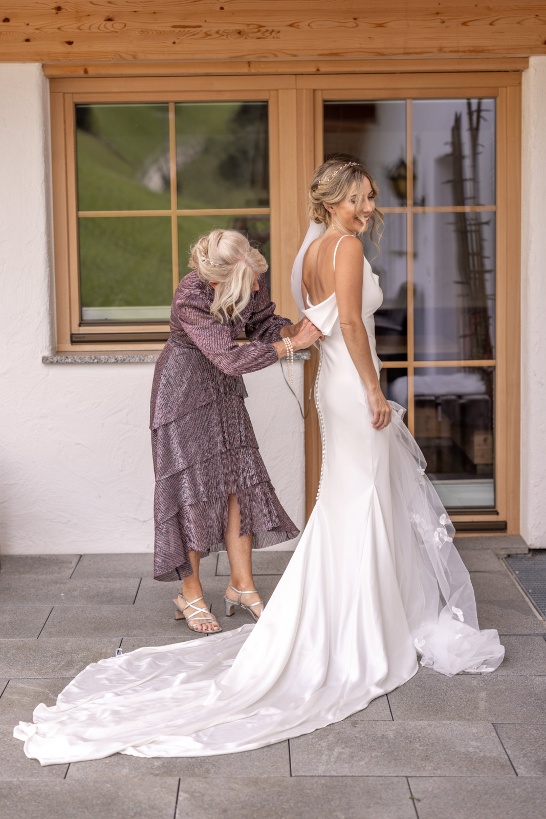 mother helps bride to put on her wedding dress